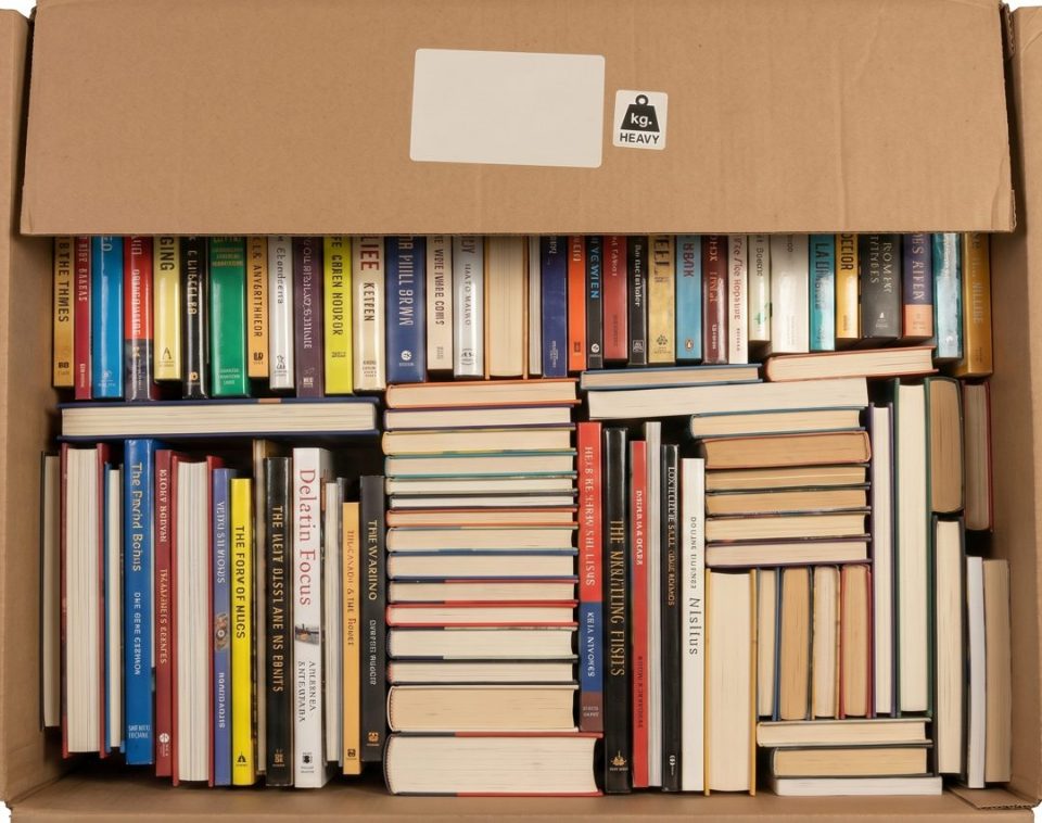Top-down view of an open moving box packed with paperback and hardcover books